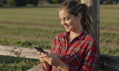 Young farmer woman creating her dating profile on a smartphone by a pasture fence