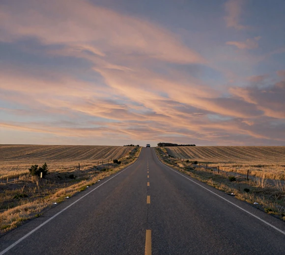 Long straight Kansas prairie highway at dusk with wheat stubble fields and dramatic sky - rural dating Kansas